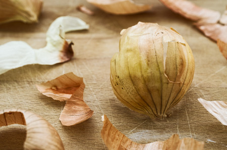 Concept of food preparation. Brown onion peelings on brown texture background, chefs knife with wooden handle on a wooden cutting board in the backgroundの写真素材