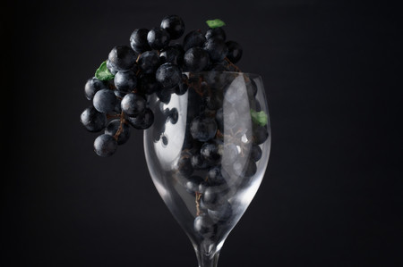 Concept of food processing. Franc variety grapes in and hanging over red wine glass against brown fabric background. Selective focus on front grapes hanging over glass.の写真素材