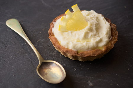 Delicious dessert fresh cheese and lemon tart decorated with lemon slice on dark stone slate. Selective focus on lemon slice. Concept of Home baking. Concept of home made desserts.の写真素材