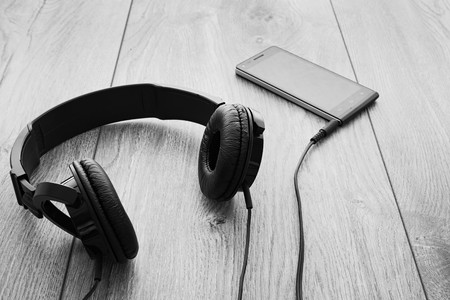 Black smartphone and black headphones on wood background. Selective focus on right earpiece of headphones. Black and white.の写真素材
