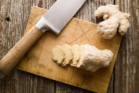 Sliced spice root, ginger and knife on wood cutting board rustic setting with ginger roots and sliced lemon in background. Top down view. Selective focus on front slice of gingerの写真素材