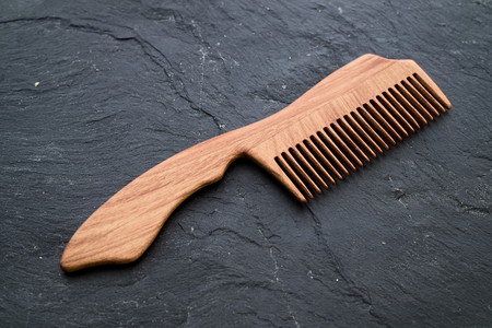 Handmade handcrafted wood haircomb on dark stone slab background. Flat lay, top down view.