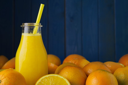 Freshly squeezed organic orange juice in bottle with colored straw and ripe organic oranges oranges agains blue wood boards background. Selective focus on straw. Concept of healthy lving. Concept of organic food. Concept of detox.の写真素材