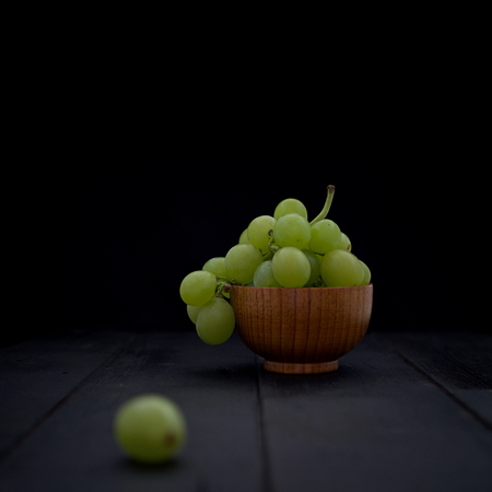 Organic white grapes in brown wood bowl on black wood boards. Selective focus on the grapes in bowl. Square crop.の写真素材
