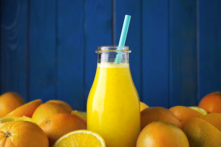Freshly squeezed organic orange juice in bottle with colored straw and ripe organic oranges oranges agains blue wood boards background. Selective focus on straw. Concept of healthy lving. Concept of organic food. Concept of detox.の写真素材