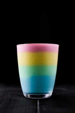 The taste of color rainbow pudding in glass on black. Layered different coloured puddings. Pink, yellow, green and blue. Selective focus. Copy space.の写真素材