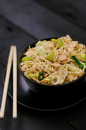 Asian food Chow Mein ramen noodles with vegetables and tofu in black bowl and plate with chopsticks on dark wood surface. Concept of asian food. Concept of chinese food.の写真素材