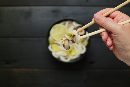 Japanese soup with udon noodles mushrooms leeks and lime. Hand grabbing food with chopsticks. Concept of eating. Hands in frame. Top down. Flat lay. Selective focus.の写真素材