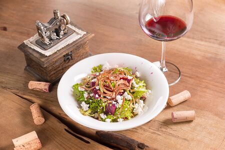 Beetroot salad mixed with lettuce, arugula and white cheese, served in a white plate with glass of red wine.の写真素材
