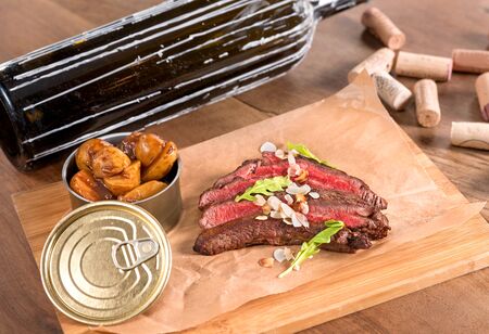 Beef flank steak with toasted almonds and saffron potatoes served in a recycled paper on a wooden board.の写真素材