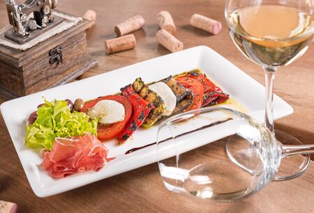 Antipasti with white wine,stewed vegetables and mozzarella served in a white plate.の写真素材