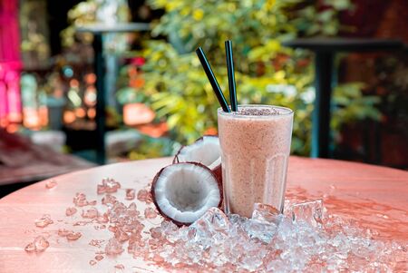 Homemade chocolate shake with coconut and chia seeds served on a wood table with ice.