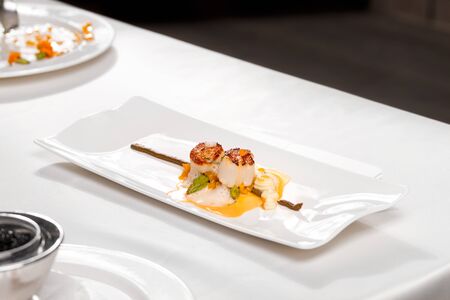 Coquilles Saint â Jacques, green asparagus and mushrooms - scallops, white mushroom cream, mushroom tortellini, green asparagus, bisque sauce and veloute, served in a white plate on a restaurant table.の写真素材