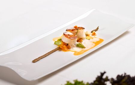 Coquilles Saint â Jacques, green asparagus and mushrooms - scallops, white mushroom cream, mushroom tortellini, green asparagus, bisque sauce and veloute, served in a white plate on a restaurant table.の写真素材