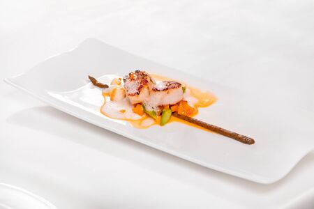 Coquilles Saint â Jacques, green asparagus and mushrooms - scallops, white mushroom cream, mushroom tortellini, green asparagus, bisque sauce and veloute, served in a white plate on a restaurant table.の写真素材