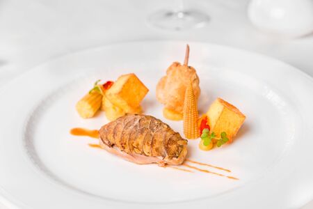 Quail in herbal Jus and variation of corn - quail with royal mushroom flakes, herb Jus, polenta cubes, glazed mini corn and corn cream, served in a white plate.の写真素材