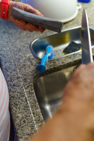 A woman sharpening a knife over the sink in the kitchenの写真素材