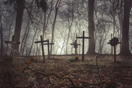 Group of an old graves on traditional Christian European cemetery. Halloween wallpaper. Rest in peace. Scary graveyard with foggy background. Close up of aged crosses tomb stones on grave yard in mistの写真素材