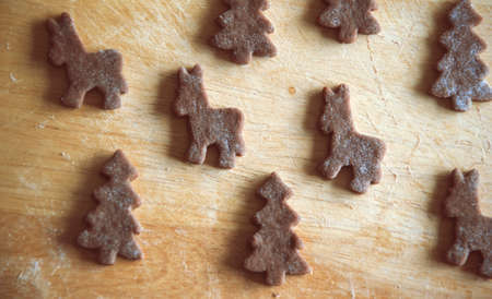 Close up of raw dough for gingerbread cookie on the kitchen table. Baking homemade Christmas cookies. Cutting out a ginger bread x-mas symbols with cutters, Top view. Preparing to celebrate Christmasの写真素材