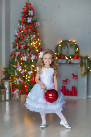 Young beautiful girl in blue white elegant evening dress near christmas tree and presents on a new year eveの写真素材