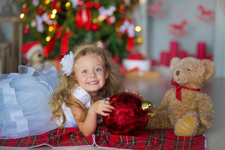 Young beautiful girl in blue white elegant evening dress on floor near christmas tree and presents on a new year eveの写真素材