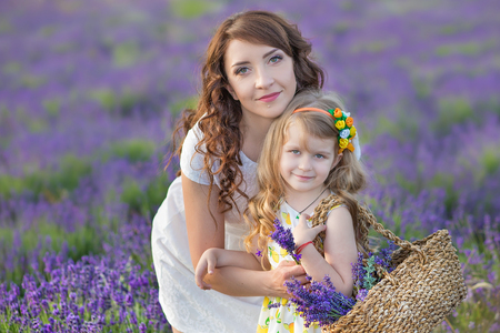 Young mother with young daughter smiling on the field of lavender .Daughter sitting on mother hands.Girl in colorful dress and mother in dark blue dressの写真素材