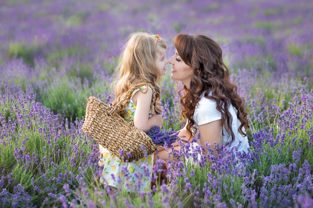 Young mother with young daughter smiling on the field of lavender .Daughter sitting on mother hands.Girl in colorful dress and mother in dark blue dressの写真素材