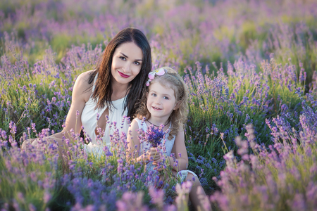 Young beautiful lady mother with lovely daughter walking on the lavender field on a weekend day in wonderful dresses and hatsの写真素材