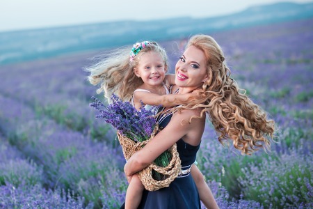 Young mother with young daughter smiling on the field of lavender .Daughter sitting on mother hands.Girl in colorful dress and mother in dark blue dressの写真素材