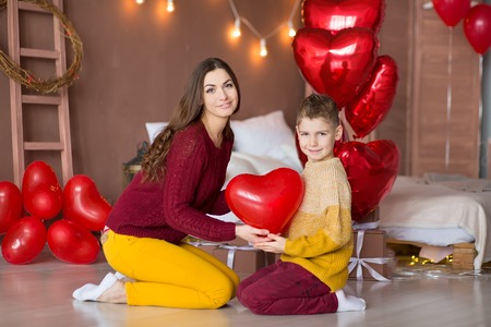 Beautiful cute young brunette mom mother with her teenager handsome boy holding each other and happy together.Woman in yellow pens and red sweeterの写真素材
