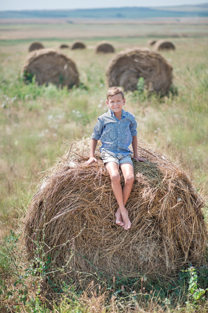 Attractive boy sitting on a haystack and smiling.の写真素材