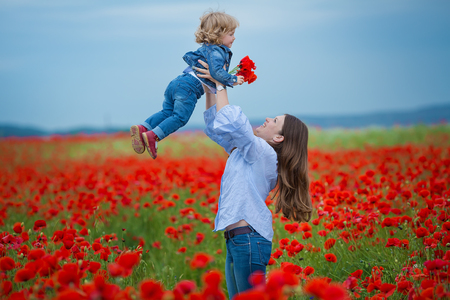 beautiful young woman with child girl in poppy field. happy family having fun in nature. outdoor portrait in poppies. mother with daughter. summer time.の写真素材