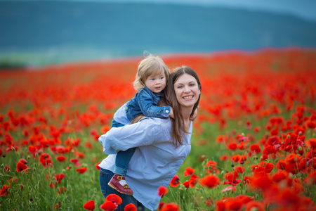 beautiful young woman with child girl in poppy field. happy family having fun in nature. outdoor portrait in poppies. mother with daughter. summer time.の写真素材