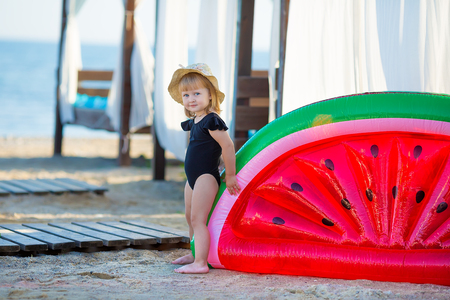Summer lifestyle portrait of pretty girl swimming posing on the back on the inflatable watermelon in the ocean, wearing stylish bikini swim wear in black and hat. Relaxing and enjoying lifeの写真素材