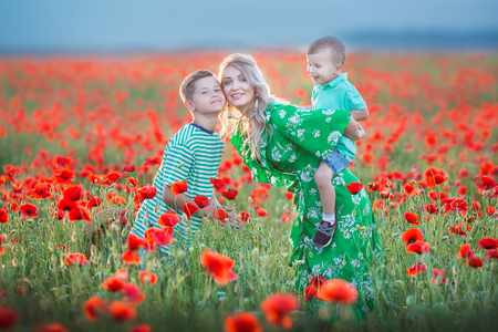 Mother with son in poppies enjoying life at sunset. Happy family summer vacation. Pretty brunette with long healthy hair holding little boy. Carefree young mom over red field. Countryside landscapeの写真素材