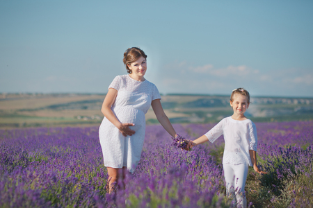 Young beautiful lady mother with lovely daughter walking on the lavender field on a weekend day in wonderful dresses and hatsの写真素材