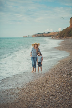 Family lovely scene of beautyful mother posing kissing her cute handsome son on beach sea side during summer vacation on ocean resort with sand cliff landscape.の写真素材