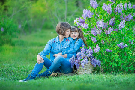 Cute adorable beautifull mother lady mom woman with brunette girl daughter in meadow of lilac purple bush.People in jeans wearの写真素材
