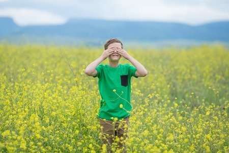 Happy cute handsome little kid boy on green grass lawn with blooming yellow dandelion flowers on sunny spring or summer day. Little boy dreaming and relaxing collecting a bouquet.の写真素材