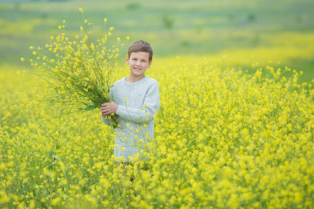 Happy cute handsome little kid boy on green grass lawn with blooming yellow dandelion flowers on sunny spring or summer day. Little boy dreaming and relaxing collecting a bouquet.の写真素材
