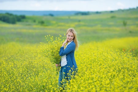 Genuine cute lady woman in meadow of yellow flowers sniffing flower bouquet. Attractive beautiful young girl enjoying the warm summer sun in a wide green and yellow meadow Stylish dressedの写真素材
