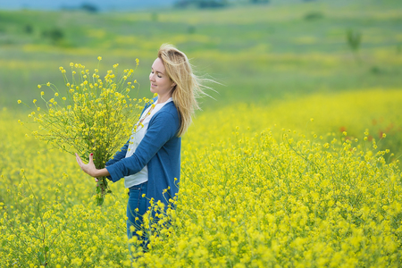 Genuine cute lady woman in meadow of yellow flowers sniffing flower bouquet. Attractive beautiful young girl enjoying the warm summer sun in a wide green and yellow meadow Stylish dressedの写真素材