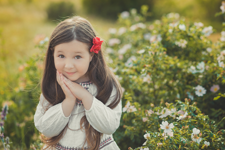 Girl with brunette hair and brown eyes stylish dressed wearing rustic village clothes white shirt and red pants on belt posing with flowers in forest meadow.の写真素材