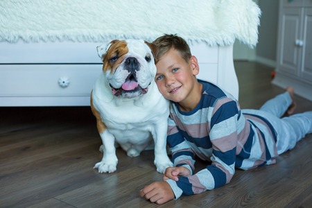Handsome Young Boy kid wearing cozy pajamas Playing with His english funny bull Dog on the floor enjoy life time weekend hanging each other with love and tender.の写真素材