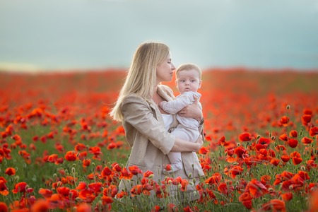 Happy motherhood. Mom and son daughter are playing in the field of flowering red poppies.の写真素材
