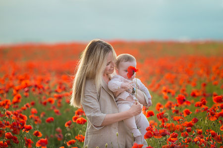Happy motherhood. Mom and son daughter are playing in the field of flowering red poppies.の写真素材