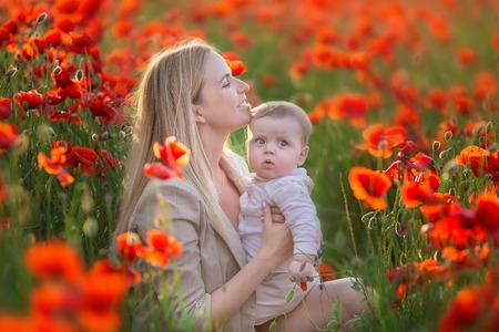 Happy motherhood. Mom and son daughter are playing in the field of flowering red poppies.の写真素材