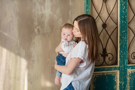 Happy Mothers Day. Adorable happy woman with baby posing in stylish modern studio decorations. Design element for card, poster, banner, and other useの写真素材
