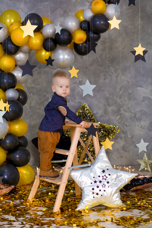 Handsome boy posing on party decorations with huge big golden star. Grey background. silver stars and different balloonsの写真素材