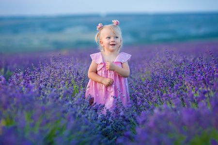 Cute little girl in airy pink dress posing standing on a lavender field and looking to clouds.の写真素材